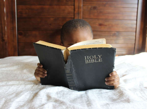 Child sitting on a bed reading the Bible