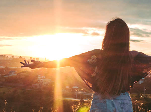 Woman with arms outstretched towards a sunset